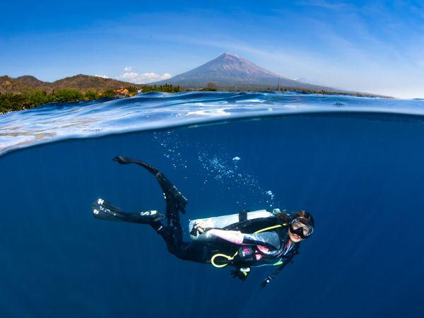 Asian diver with volcano backdrop split shot in Bali