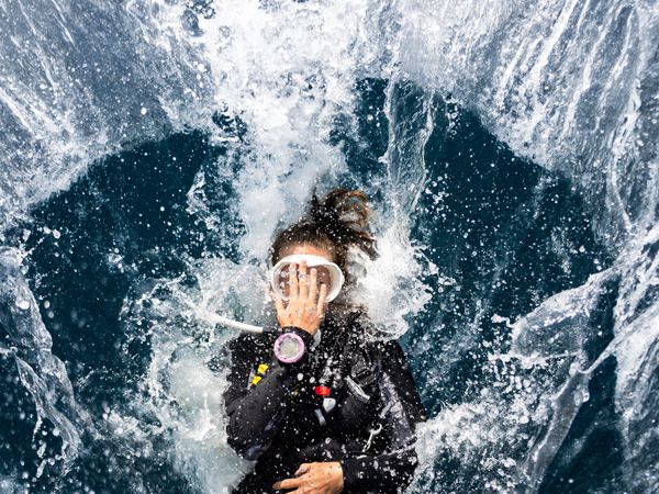 Female diver performing back roll entry with dive computer